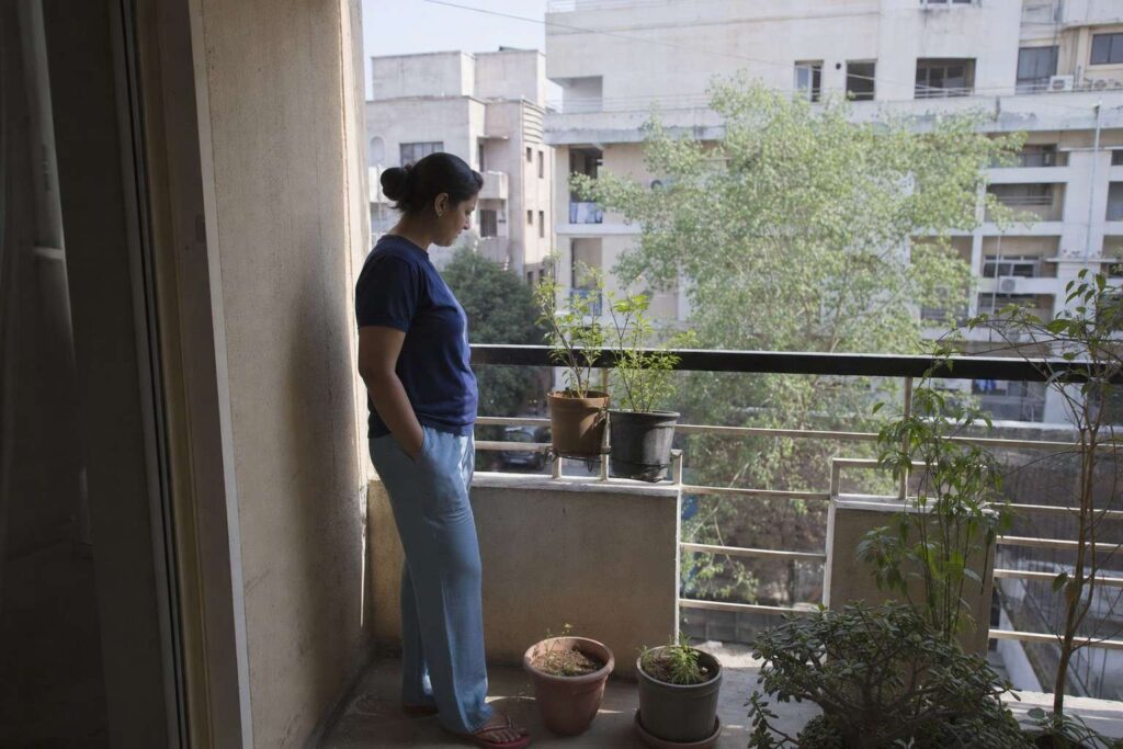 A person standing on a small apartment balcony with a few starter pots in morning light