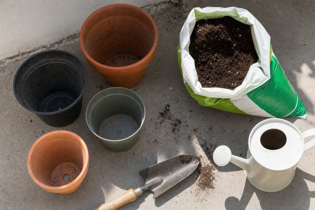 A beginner's container gardening setup with empty pots, a bag of potting mix and a trowel on a patio