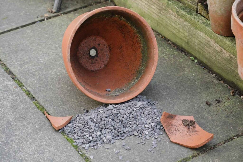 An empty terracotta pot tipped on its side showing its drainage hole, with loose gravel spilled beside it on a patio