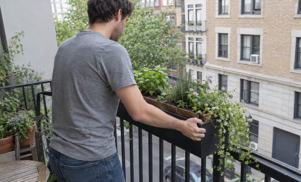 A person seen from behind fitting a planted box over a narrow apartment balcony railing