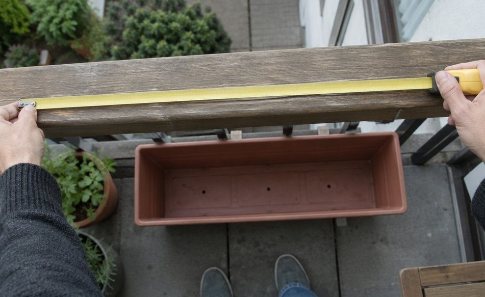 A tape measure held across the top of a balcony railing to check its width